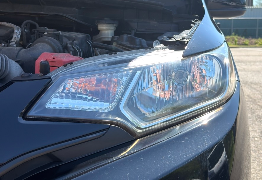 Close-up of a black car’s front headlight with the hood open, showing the engine bay.