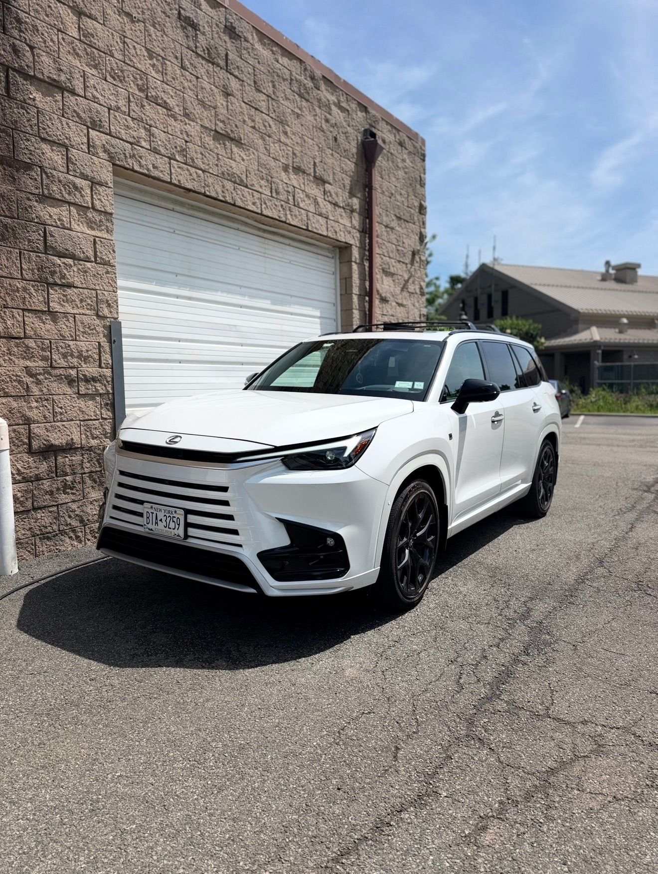 White SUV parked beside a brick building and garage door on a sunny street.