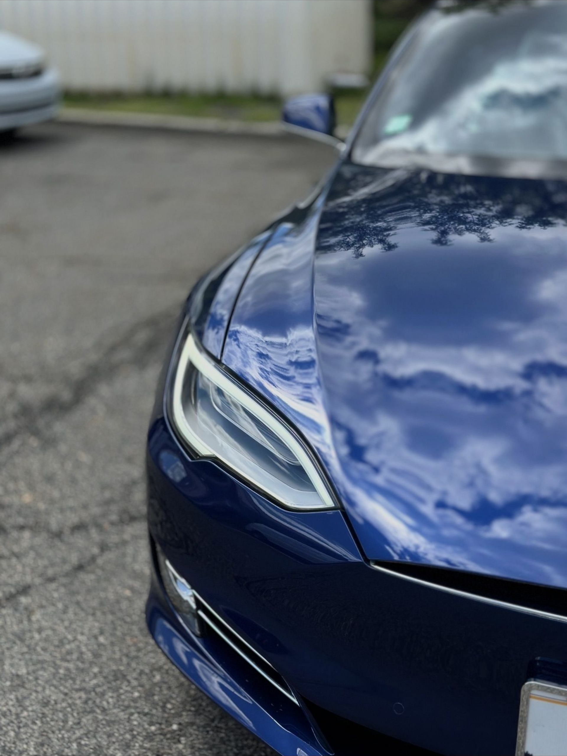 Close-up of a blue car’s front end parked on wet pavement near a fence