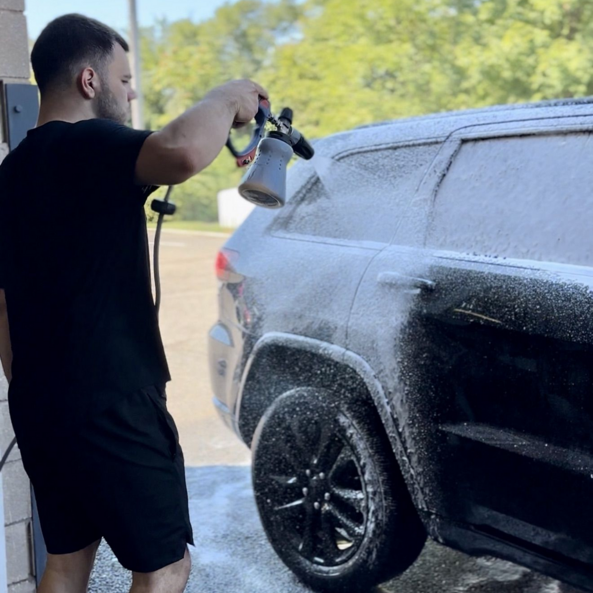 Person pressure-washing a black SUV outdoors, spraying thick foam over the side panels