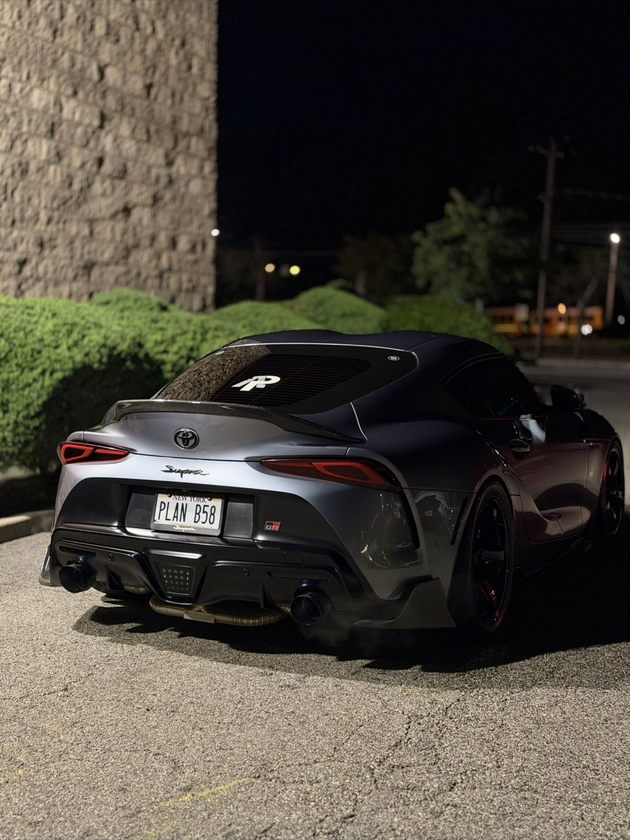 Black Toyota sports car parked at night beside a stone wall and hedge