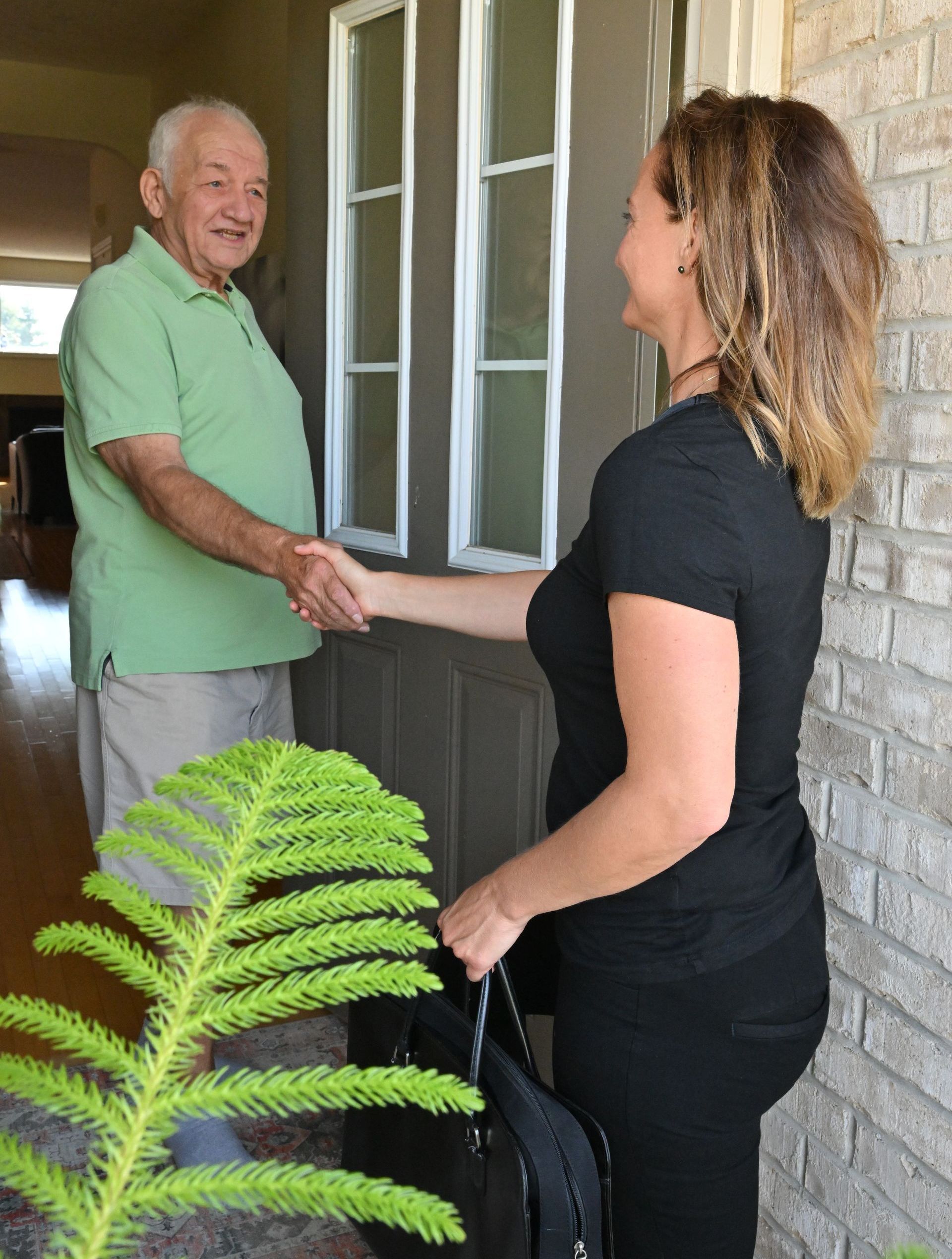 Physiotherapist greeting her client at his front door with a hand shake.