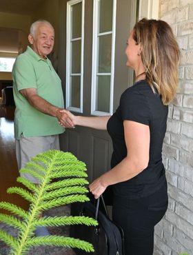 Physiotherapist greeting her client at his front door with a hand shake.