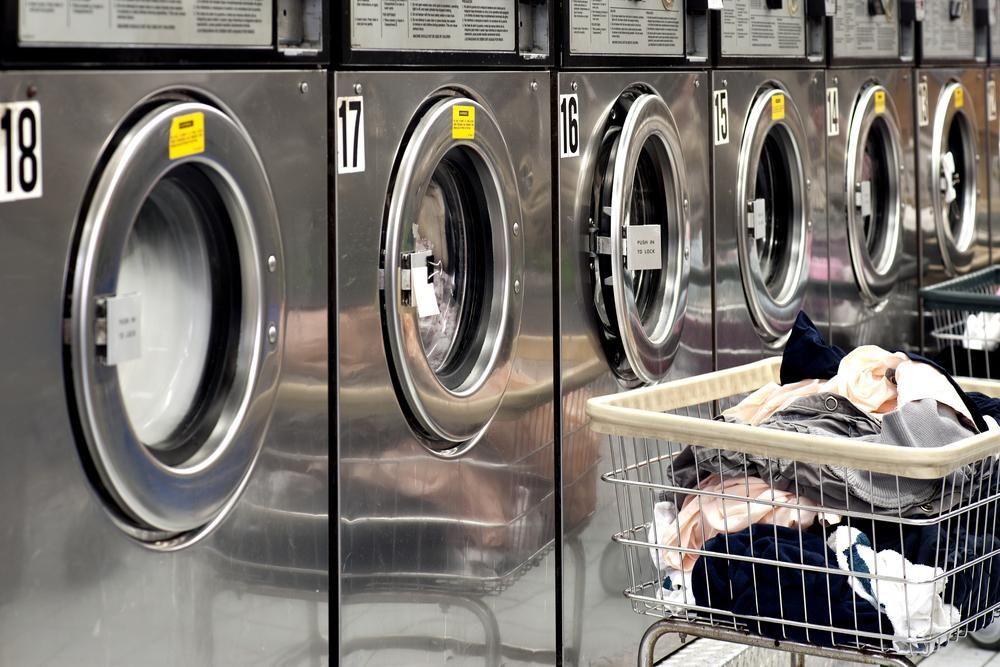 A row of washing machines in a laundromat with a basket full of clothes. — Tuncurry Washerteria In Forster, NSW