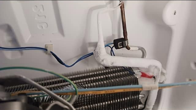Close-up of refrigerator coils and wiring inside an appliance compartment, with blue and black wires.
