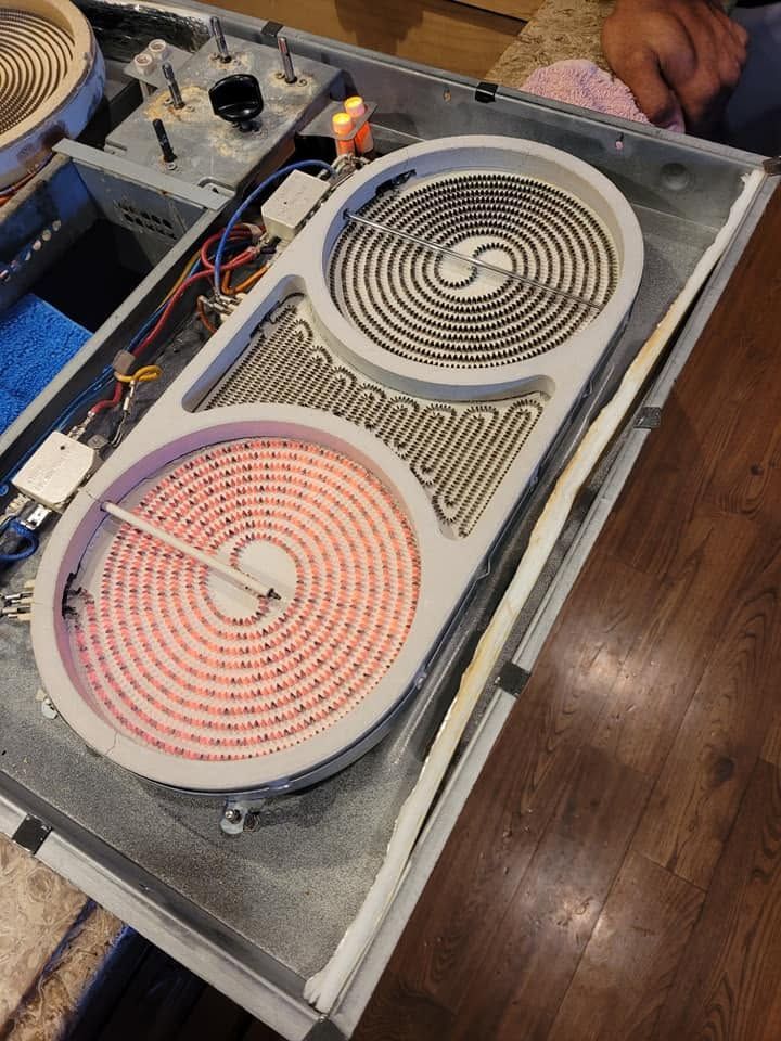 Open electric stovetop with exposed burners and wiring on a wooden floor