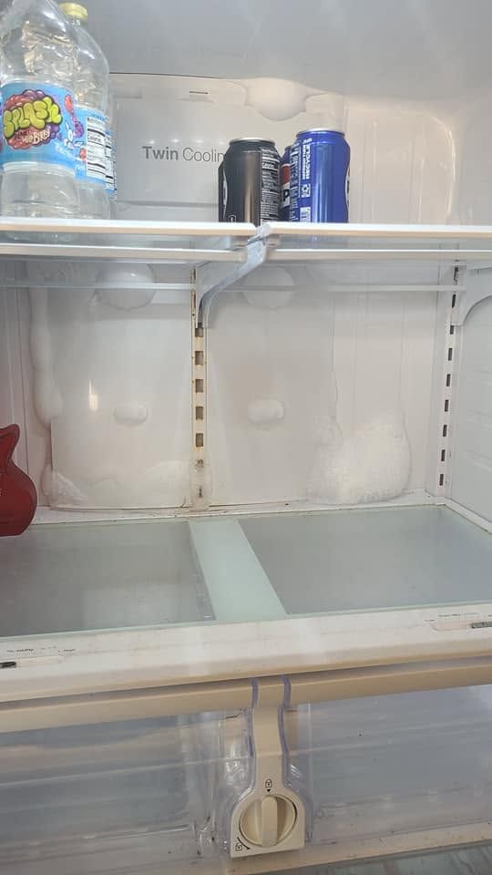 Mostly empty refrigerator with a few cans on the top shelf and a drawer below.