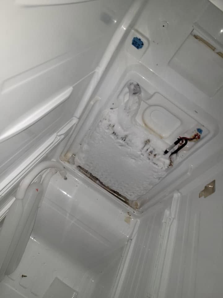 Inside a white refrigerator, the interior wall is damaged and heavily stained with rust and residue.