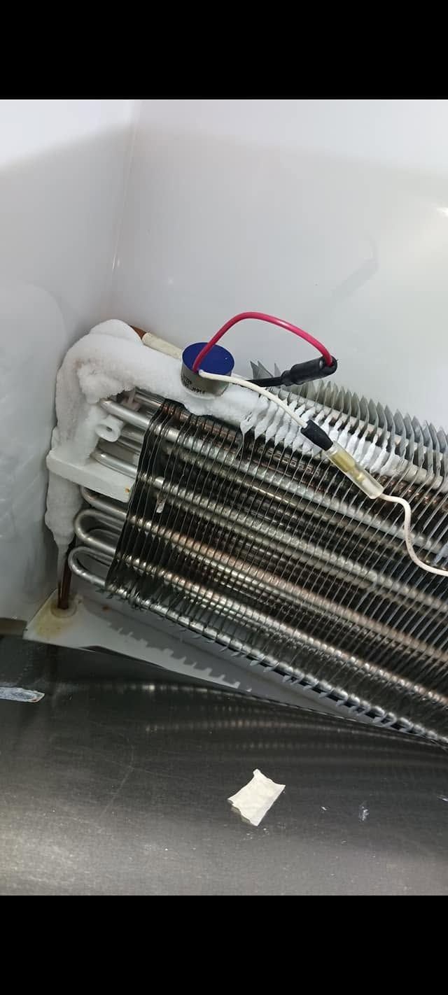Coiled metal tubes with white clips and red-blue wires inside a white appliance compartment