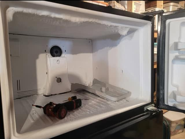 Open mini-fridge with a bottle and a cup inside on a shelf in a kitchen or garage.