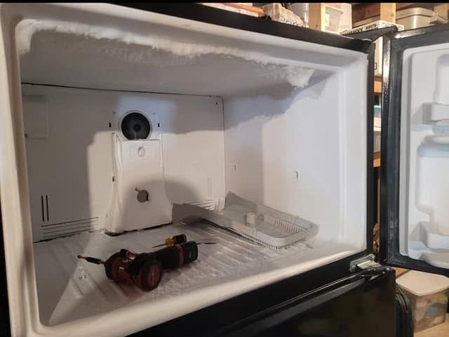 Open freezer with a bottle, sunglasses, and an ice tray inside