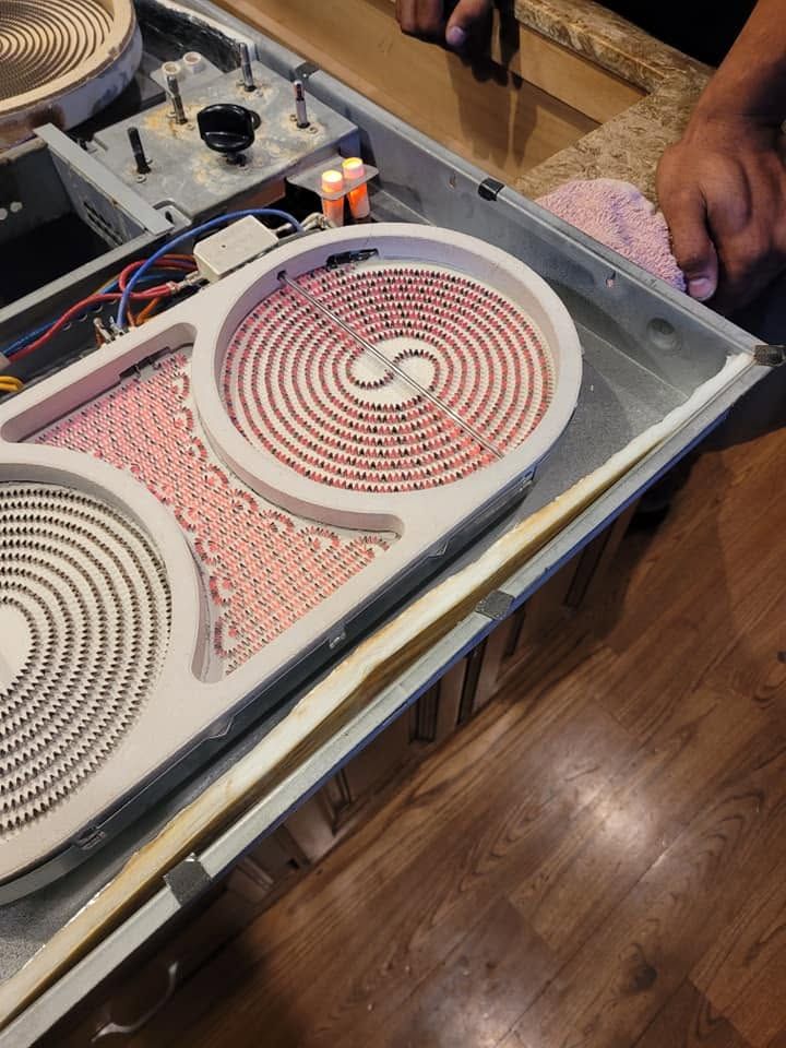 Open portable cooktop with two spiral burners and wiring exposed on a tabletop near a wooden floor