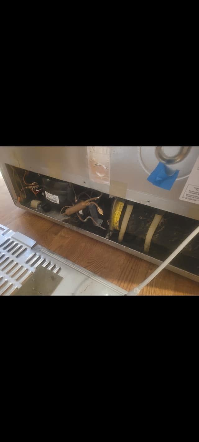 Damaged cabinet with exposed plumbing and pipes under a sink, with tools and debris on the floor