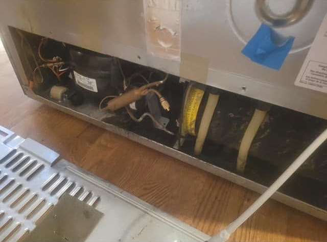 Open dishwasher base with exposed wiring, hoses, and yellow insulation beneath a kitchen counter.