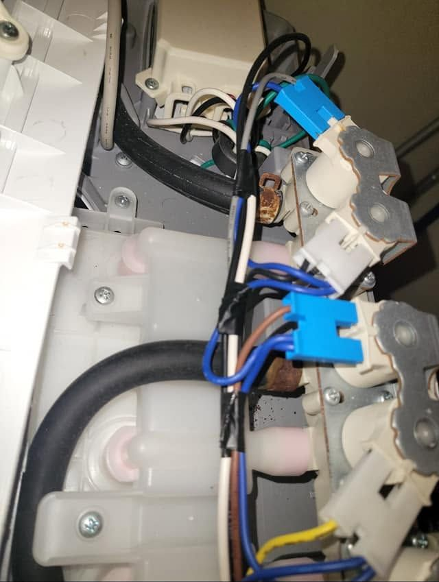 Close-up of electrical wiring, black hoses, and blue connectors inside a machine enclosure