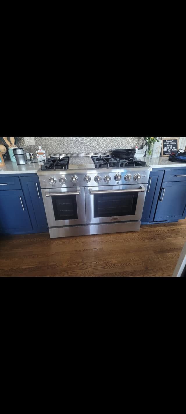 Stainless steel stove with black oven doors between blue kitchen cabinets on a wooden floor.