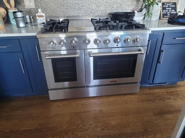 Stainless steel range between blue cabinets on a wooden kitchen floor.