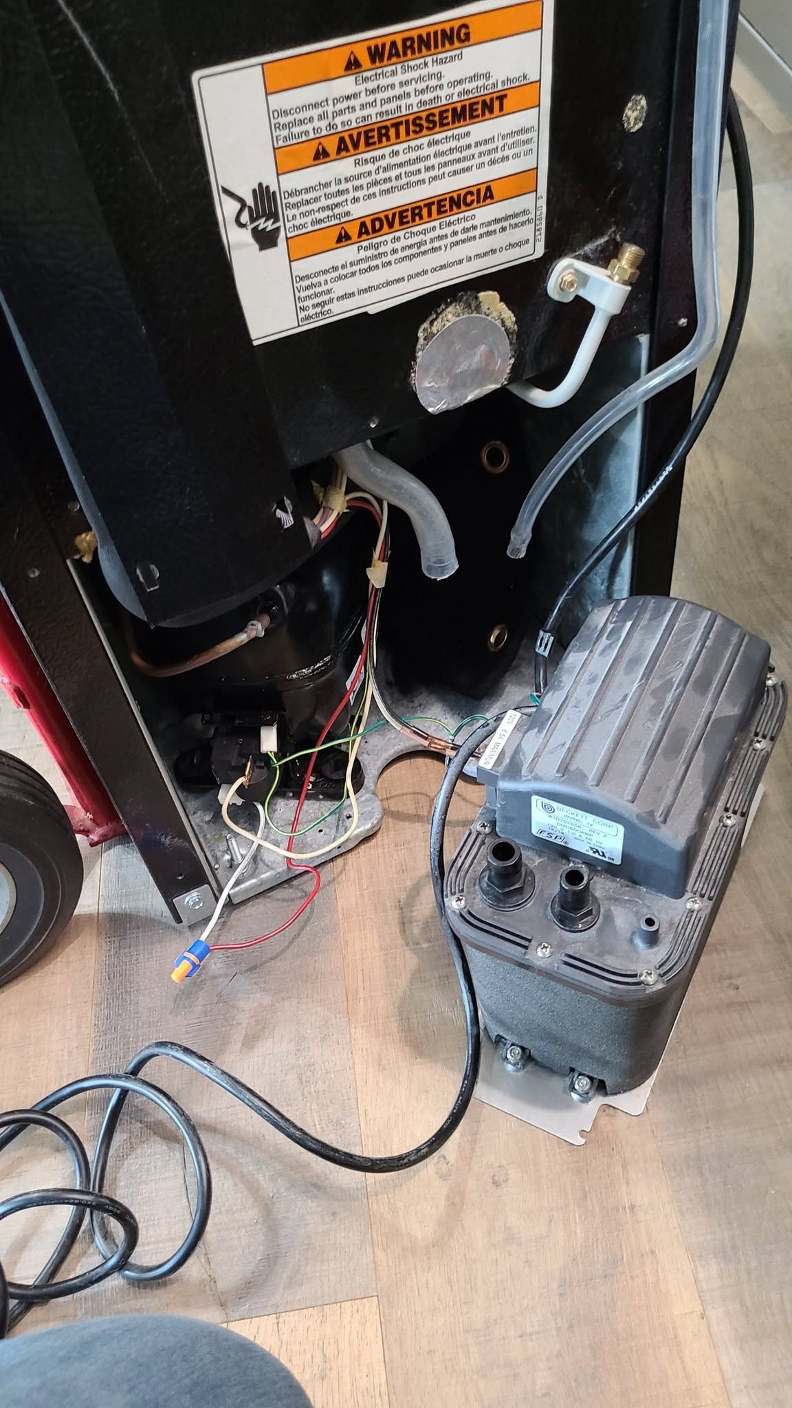 Black appliance back with hoses and wiring beside a portable air compressor on a floor.