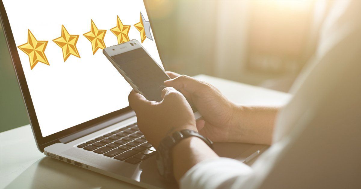 Hands using a smartphone beside a laptop with five gold stars on the screen