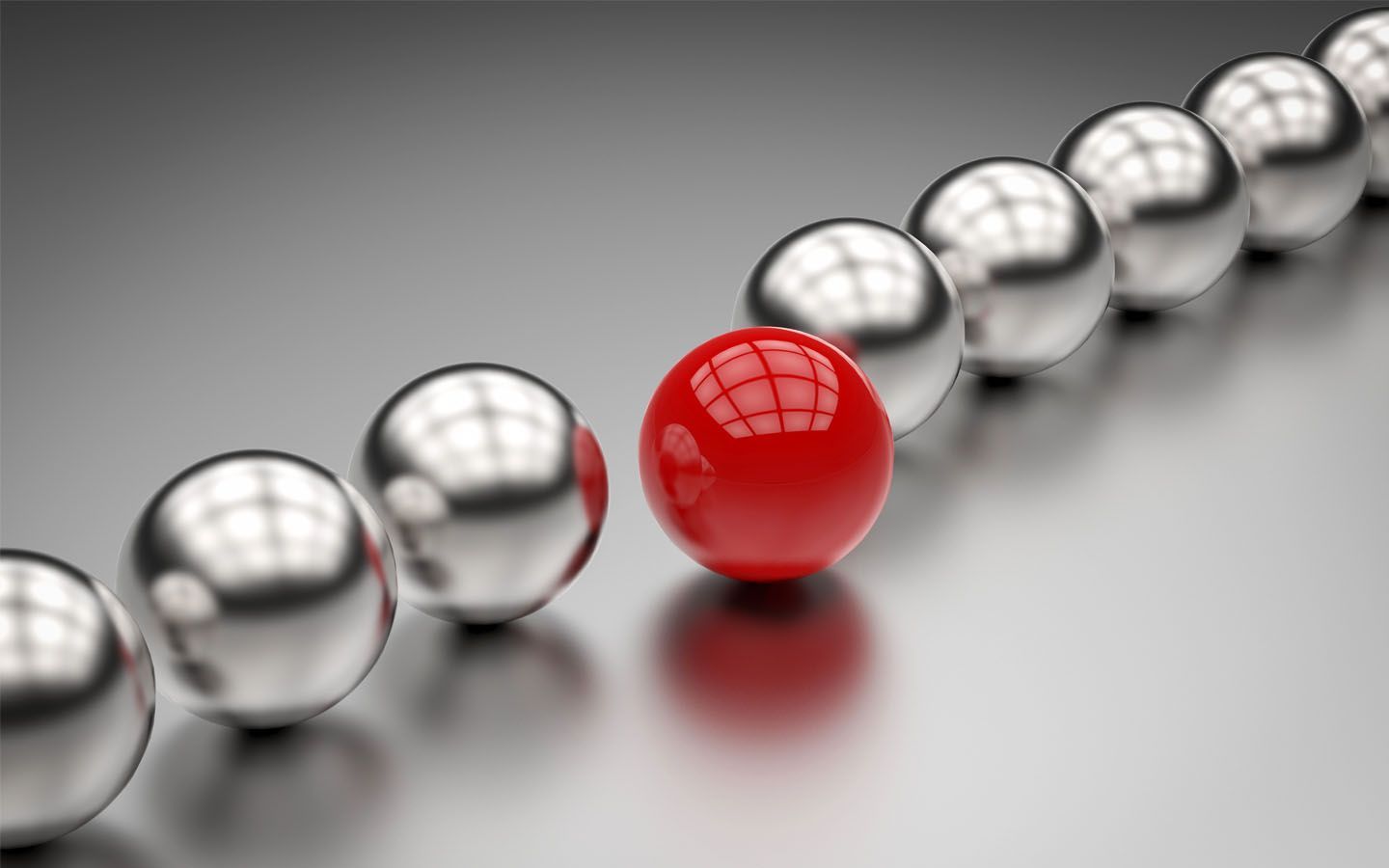 A red sphere among a row of shiny silver spheres on a reflective surface.