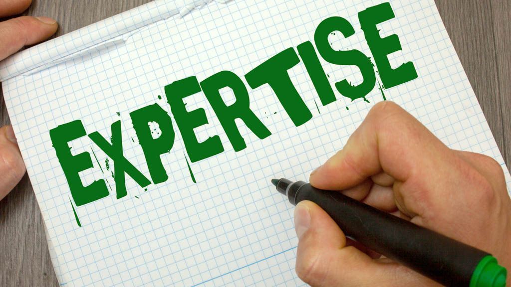 Hand writing the word “EXPERTISE” in green on graph paper with a black marker