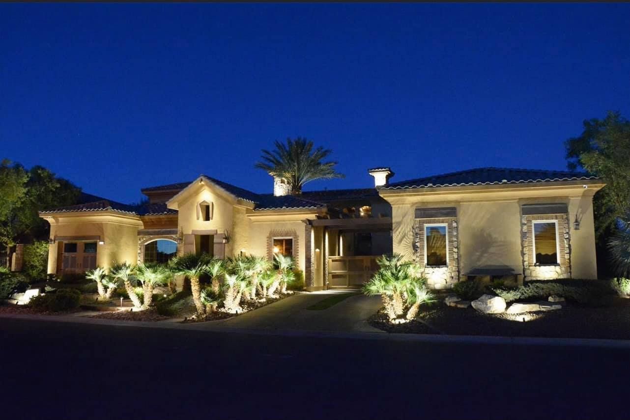 Illuminated Mediterranean-style house at night with landscaped front yard under a deep blue sky