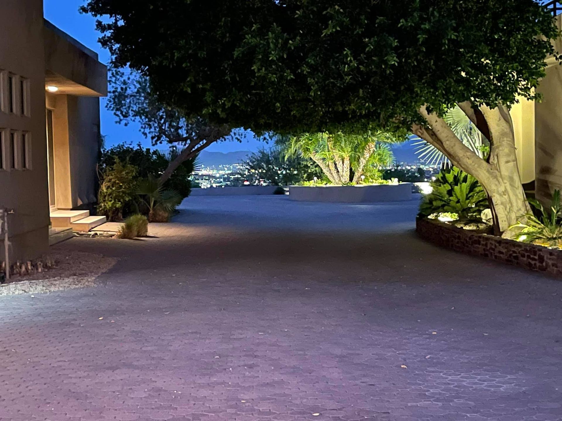 Dim driveway between buildings leading to a lit waterfront path at dusk