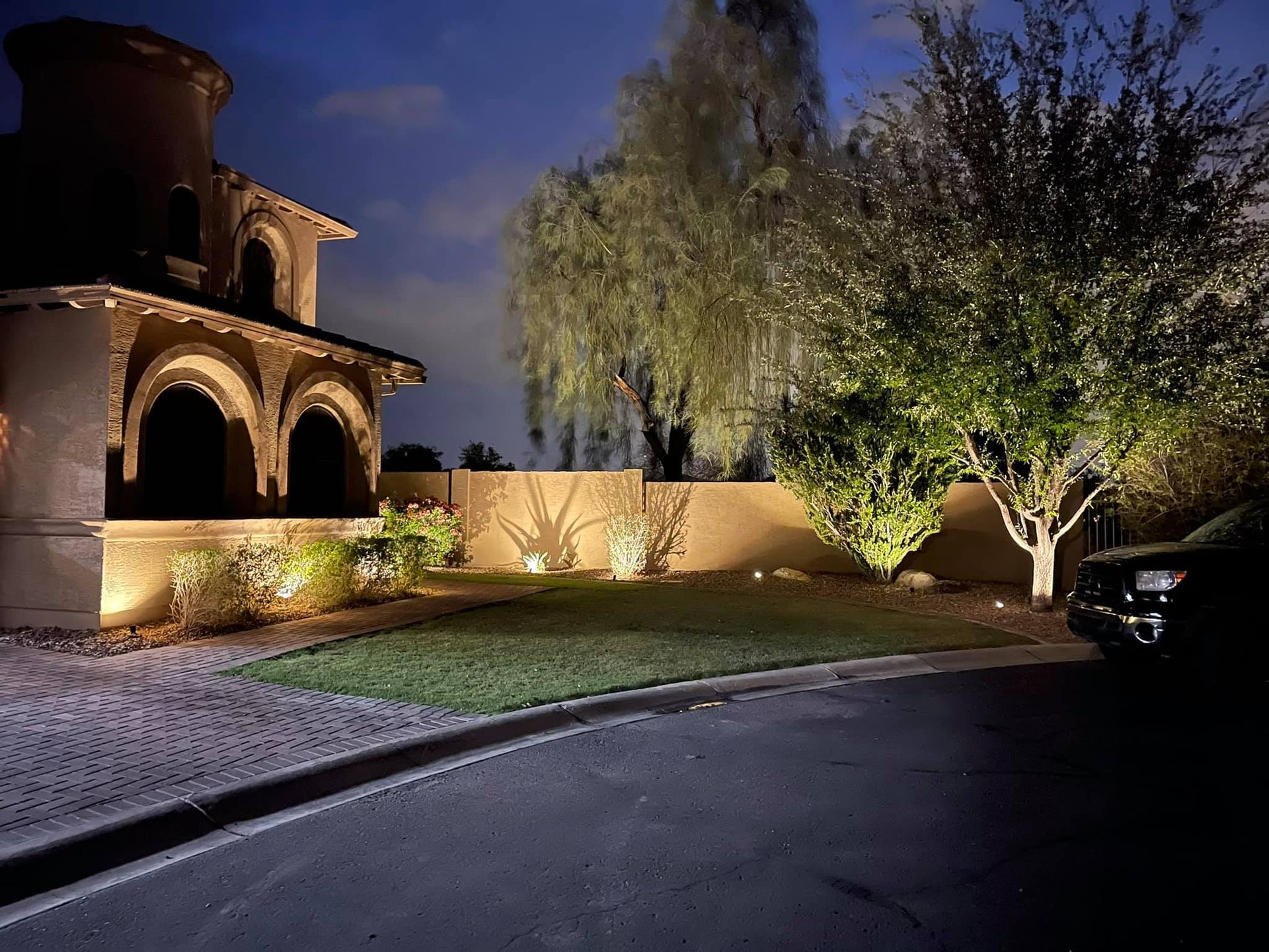 Nighttime view of a lit stucco house, arched porch, and trees along a curved driveway