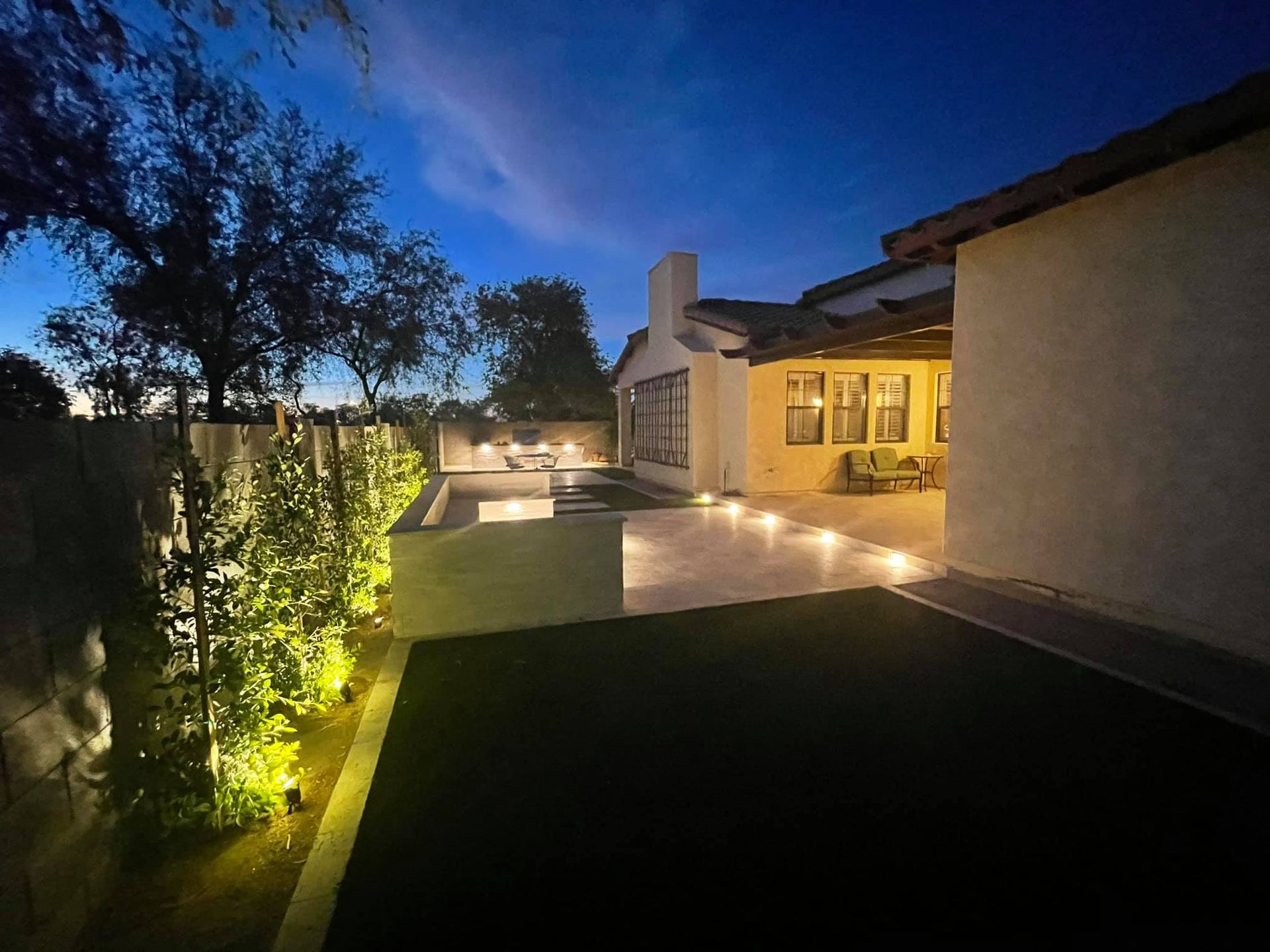 Modern house patio at dusk with warm lights, illuminated walkway, trees, and a lit outdoor seating area
