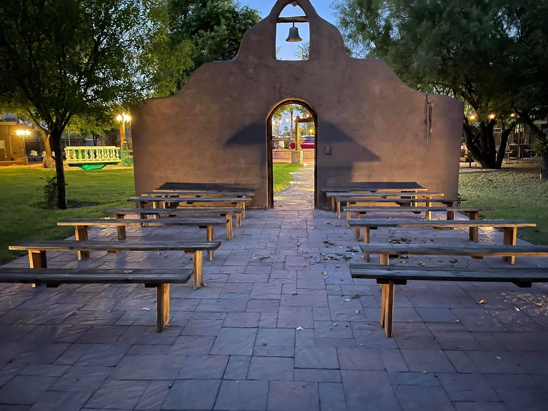 Outdoor stone chapel with benches arranged in rows in a dimly lit courtyard at dusk