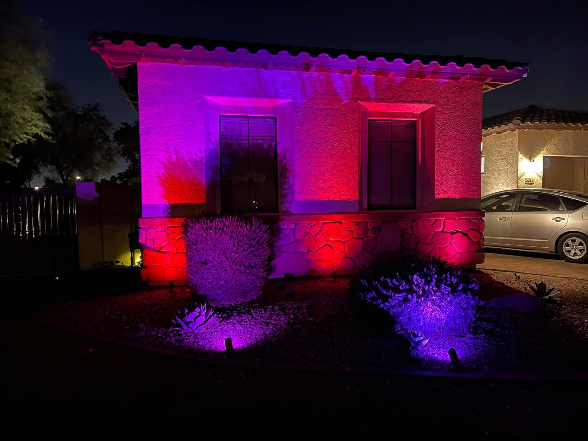 House exterior lit with bright pink and purple lights at night, with a car parked beside it