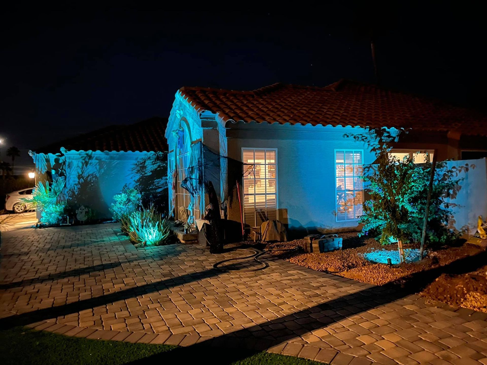 Single-story house at night, lit with blue and warm lights, with a brick driveway and desert landscaping.
