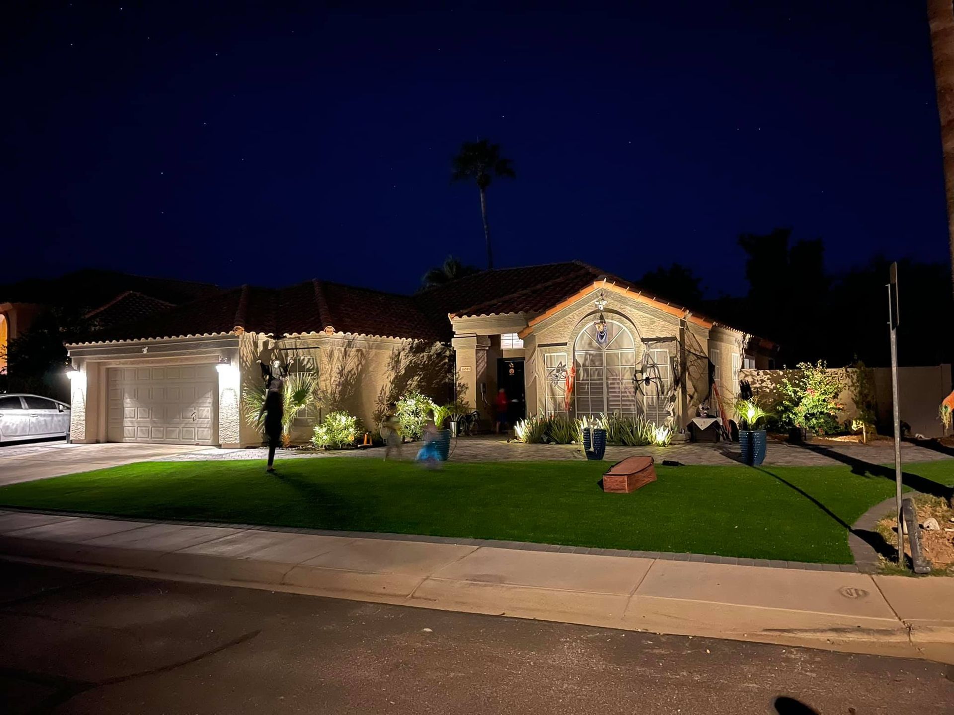 Illuminated suburban house with stone exterior, manicured lawn, and driveway at night