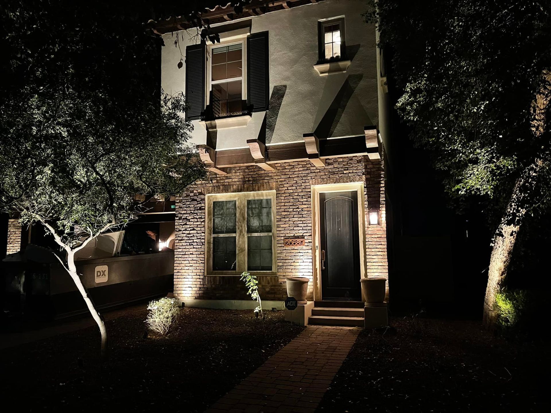 Illuminated two-story house at night with stone facade, lit windows, and trees in the yard