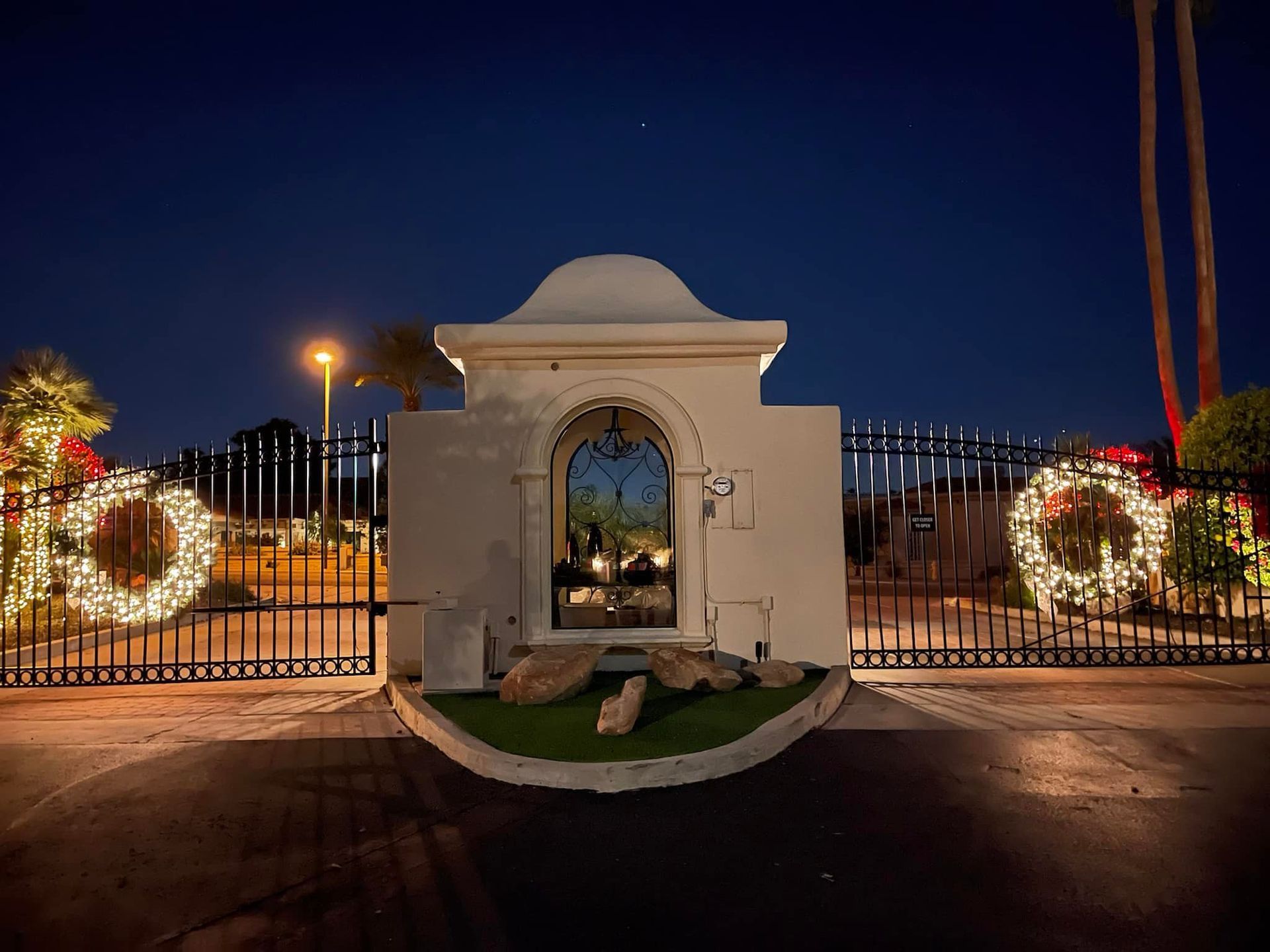 Decorated entrance gate at night, lit with holiday wreaths and lights against a dark sky