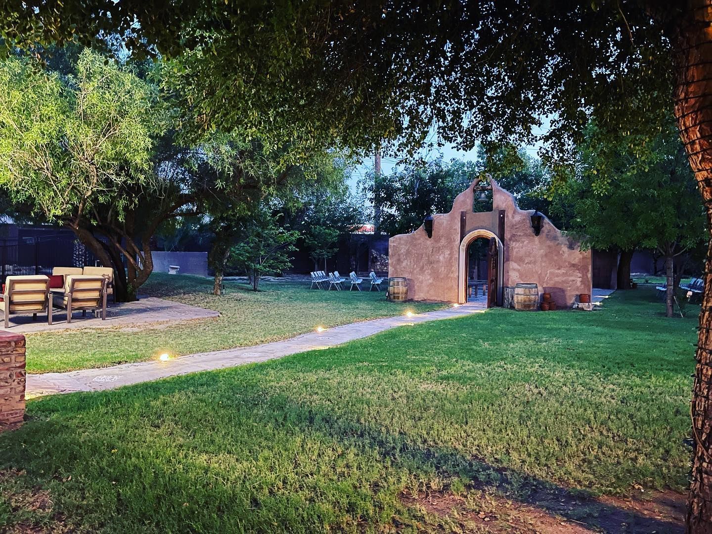 Stone outdoor oven in a grassy park with a paved path, trees, and picnic benches nearby