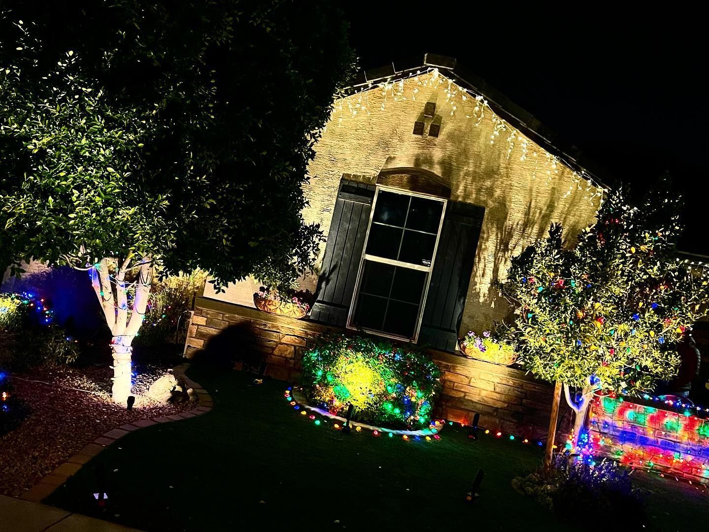 House decorated with colorful Christmas lights at night, with illuminated trees and a lit lawn.