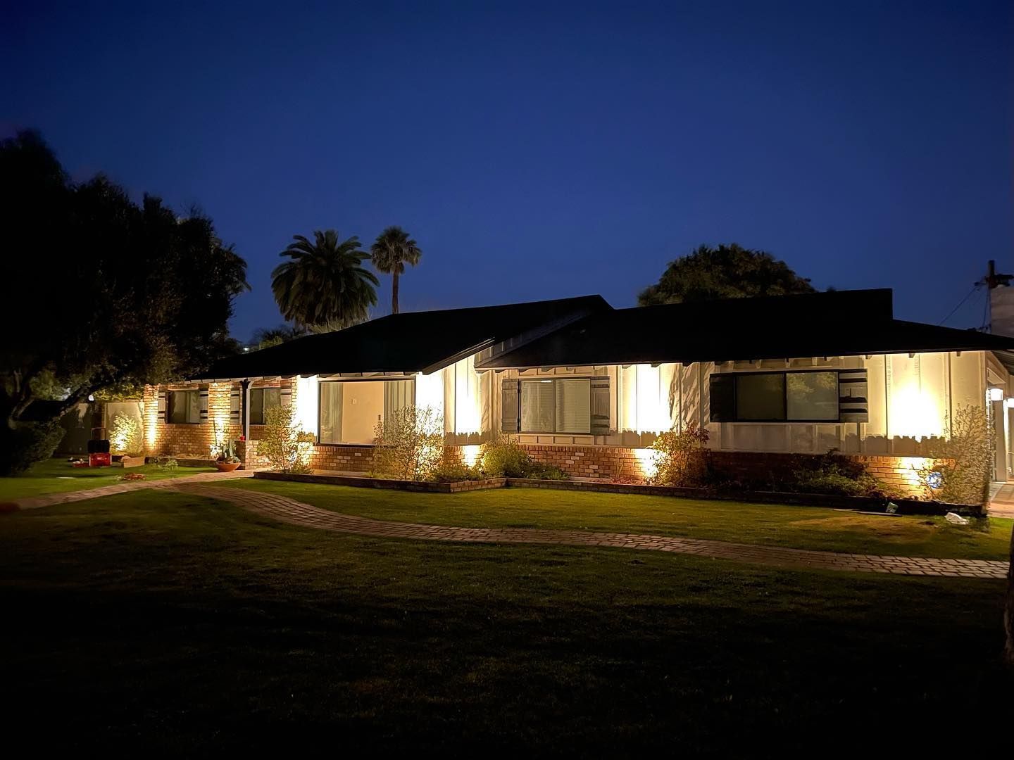 Single-story house lit warmly at dusk, with a dark lawn and deep blue evening sky.