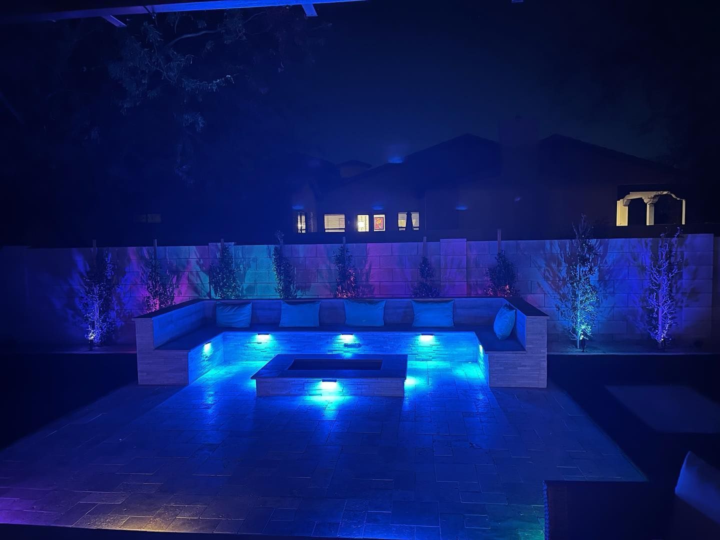 Blue-lit backyard patio with a modern seating area and illuminated pool at night