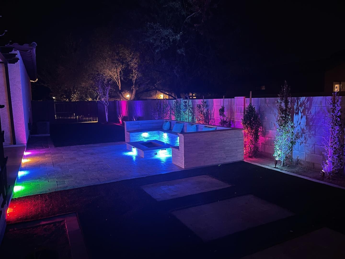 Nighttime patio with colorful LED lights, raised seating, and illuminated fence walls