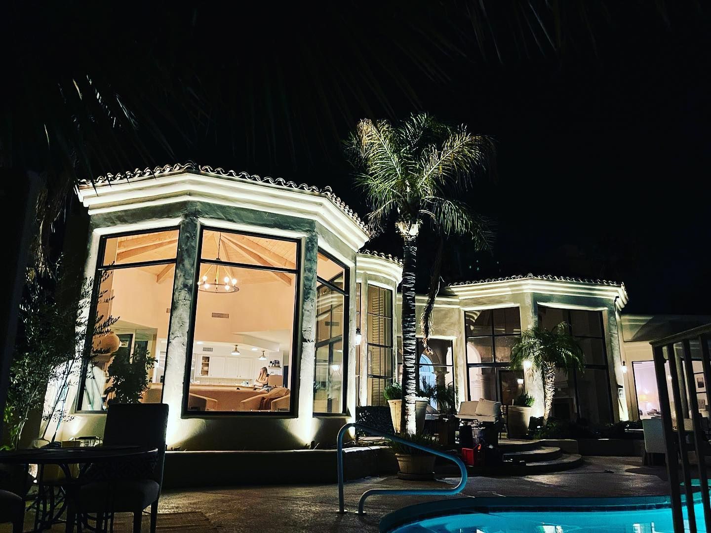Illuminated modern café at night with large windows and outdoor seating by a pool