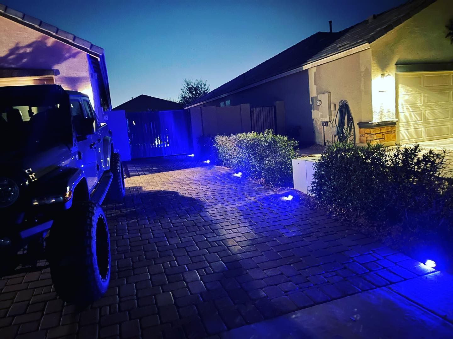 Blue-lit driveway beside a house at dusk, with a parked truck on the left.