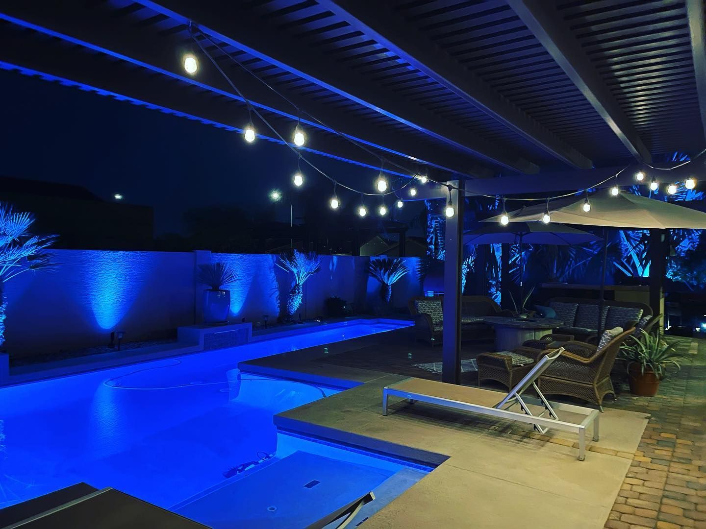 Blue-lit backyard pool area with lounge chairs under string lights at night