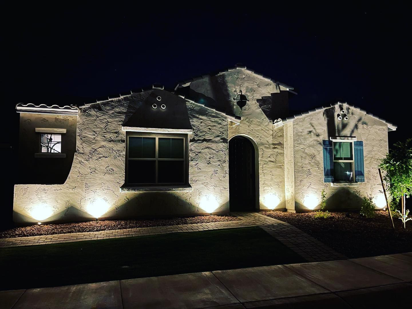 Single-story house at night, lit by warm landscape lights against a dark sky.
