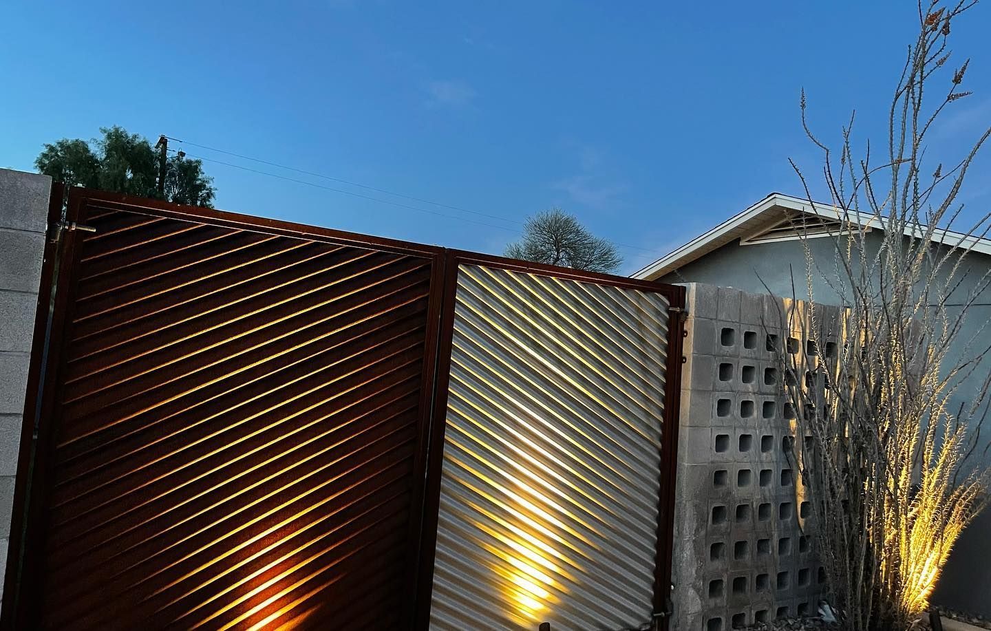 Modern outdoor fence with diagonal slats lit by warm ground lights against a blue sky