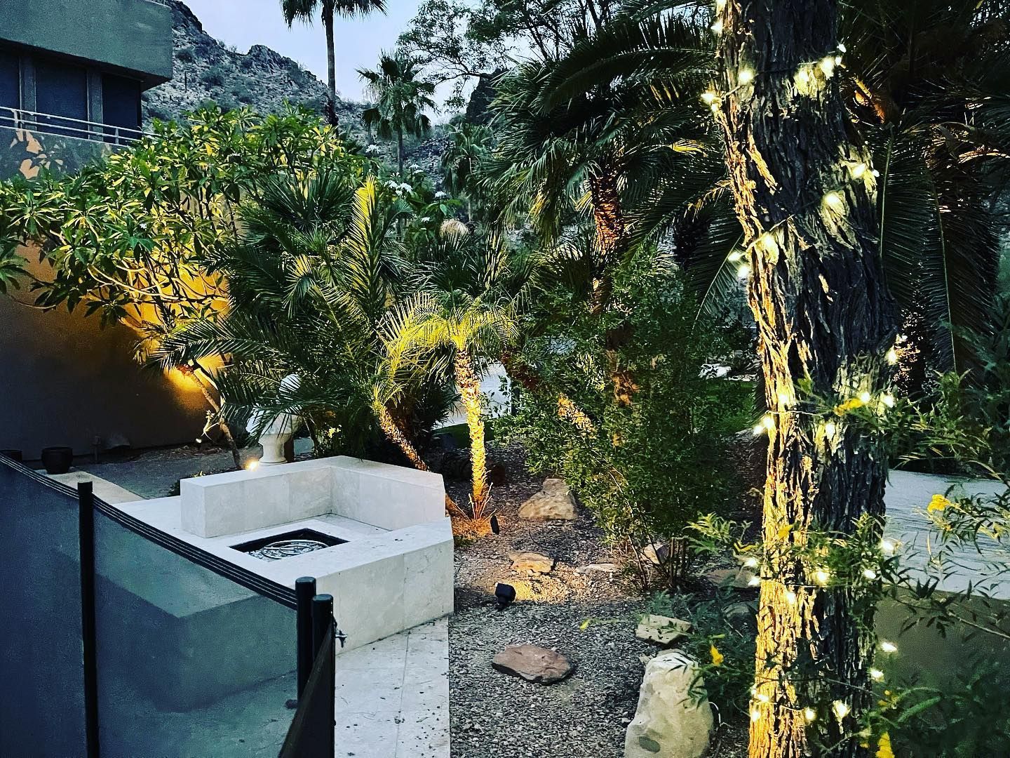 Small courtyard garden with lush trees, gravel path, and a white outdoor sink at left.