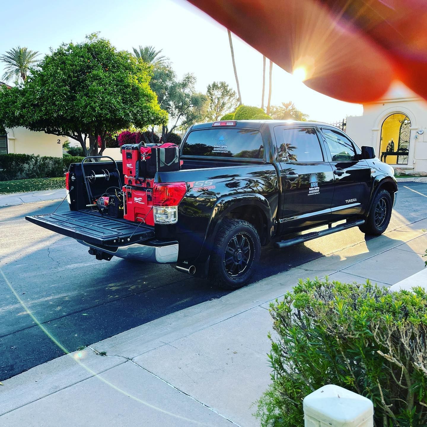 Black pickup truck with red tailgate-mounted equipment parked on a suburban street at dusk