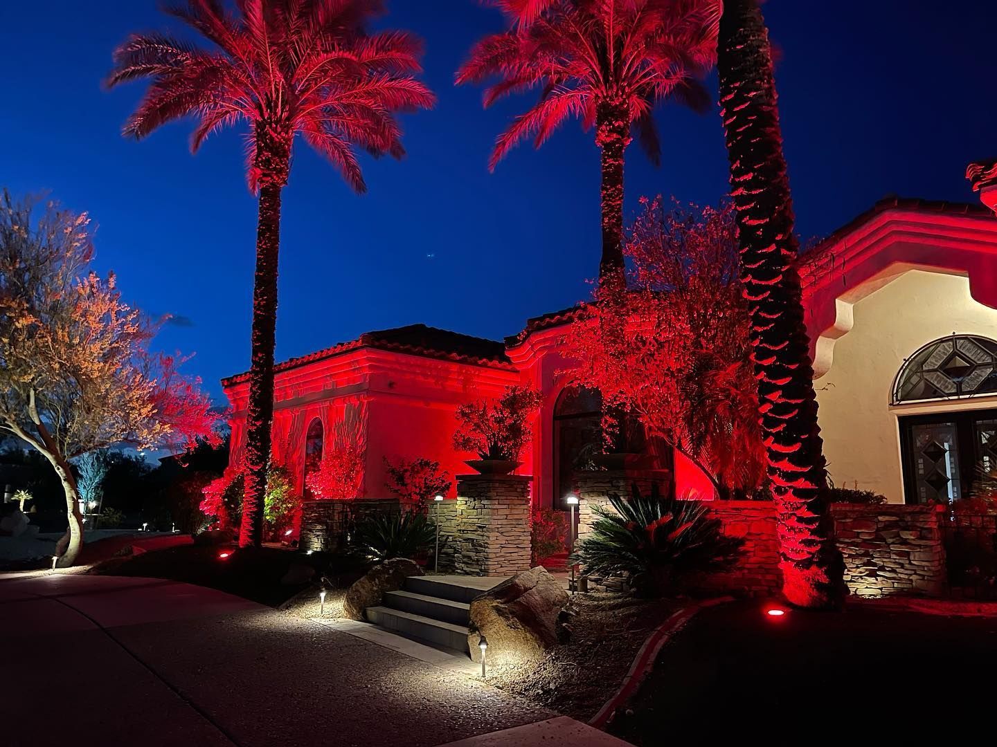 Palm-lined building illuminated in vivid red at night, with lit entrance and dark blue sky.