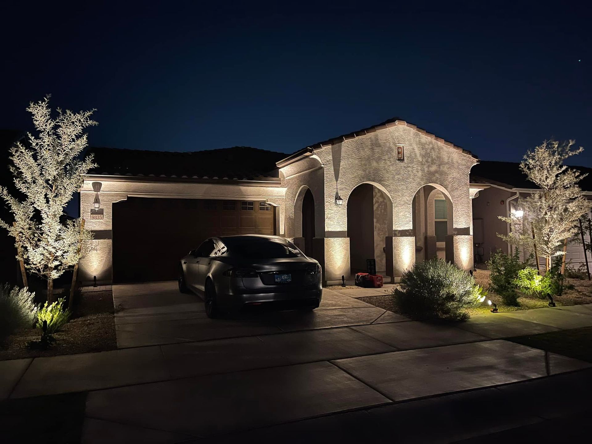 Well-lit brick house at night with two garage doors and a car parked in the driveway.