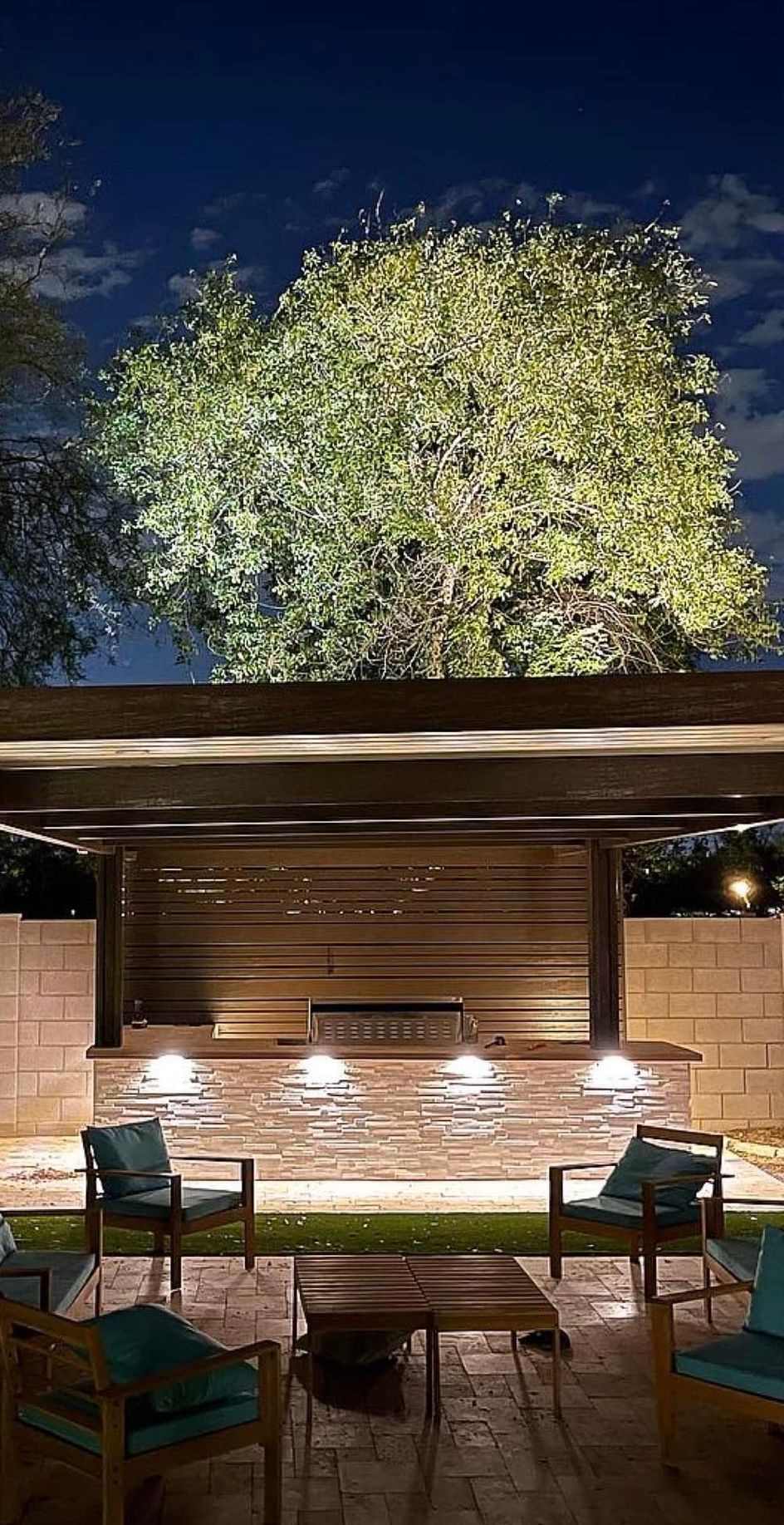 Outdoor patio with tables and chairs beneath a lit tree at dusk